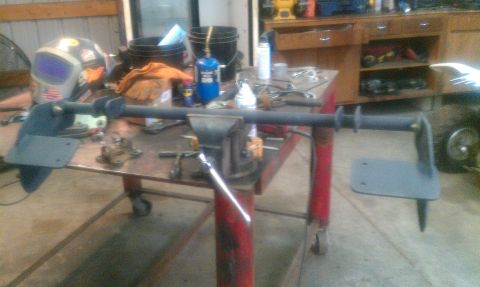 1995 Ford Bronco - A fabricated metal part is secured in a vise on a workbench, with tools and a welding mask in the background.