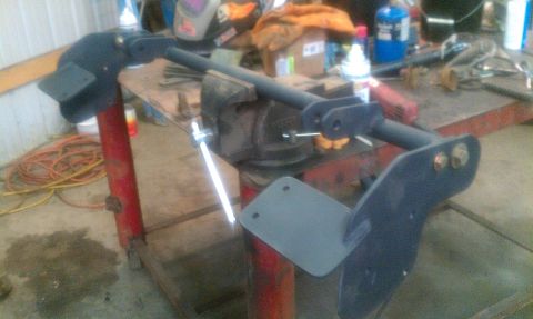 1995 Ford Bronco - A black metal suspension component is secured in a vise on a workbench, with tools and supplies in the background.