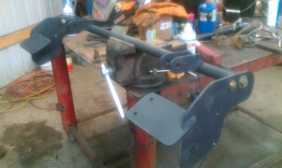 Black metal suspension part clamped in a vise on a workbench