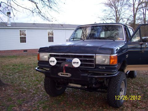 1990 Ford Bronco - A dark blue 1990 Ford Bronco is parked in a yard with the driver's door open.