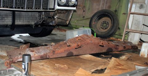 1976 Ford Ranchero - A heavily rusted metal component lies on wooden planks, with the front of a vehicle overhead.