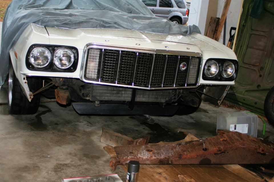 1976 Ford Ranchero front end with dual headlights and chrome grille, partially covered by a tarp