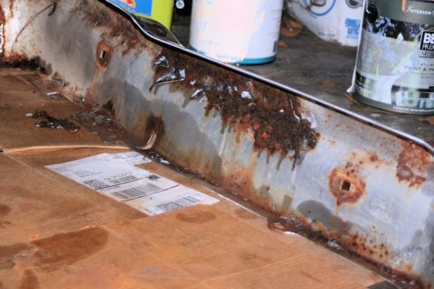 1976 Ford Ranchero - A heavily rusted metal part, possibly a bumper or undercarriage component, sits on cardboard with a shipping label.