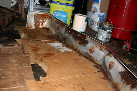 1976 Ford Ranchero - This is a rusted chrome bumper part lying on cardboard in a garage.