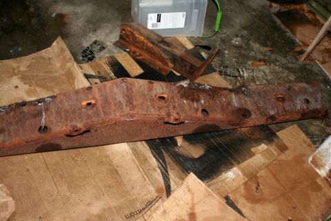 1976 Ford Ranchero - A heavily rusted metal component, possibly a frame or bumper, lies on cardboard with other metal pieces.