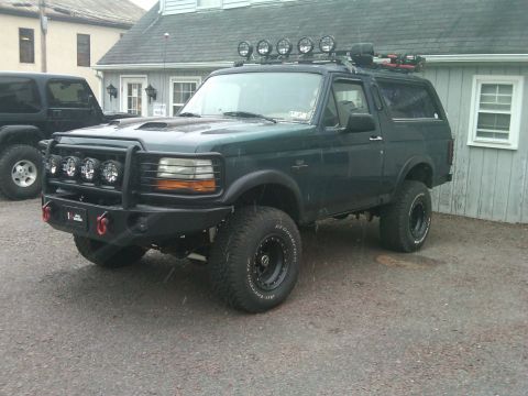 1993 Ford Bronco - This modified Ford Bronco is parked outside a building next to another SUV.