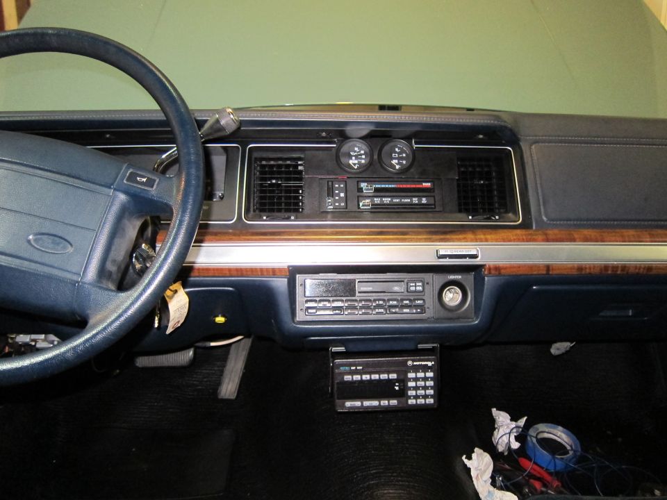 Car dashboard with steering wheel, radio, and gauges. A Motorola radio is mounted below the main dash