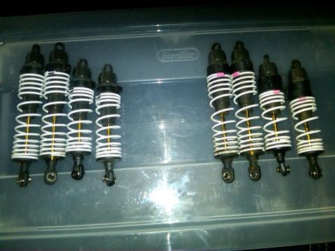 1986 Ford Bronco - Eight black shock absorbers with white springs and gold shafts are laid out in a plastic container.