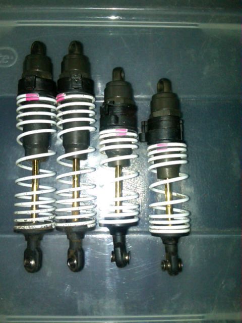 1986 Ford Bronco - Four shock absorbers are laid out in a row, showing their white coil springs and black bodies.