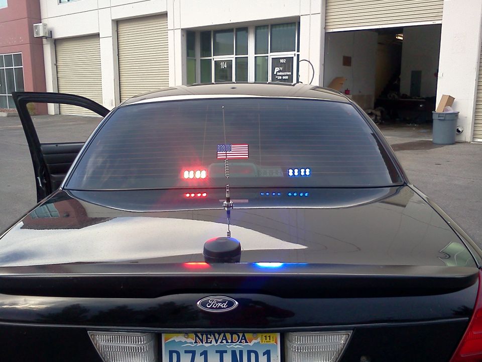 Black 2007 Ford Crown Victoria rear view with red and blue police lights on the rear window and trunk lid