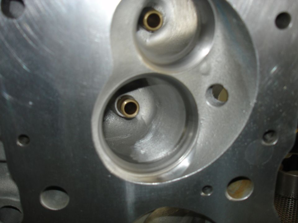 Close-up of an engine cylinder head with two valve openings. One opening has a brass insert
