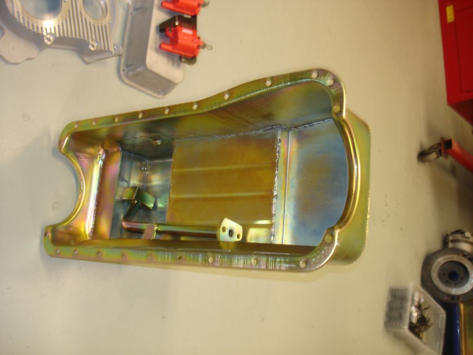 Yellow-coated metal oil pan with visible welds and internal baffles, mounted on a wall