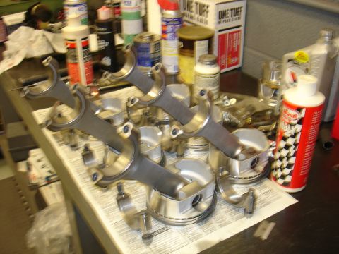 1988 Ford Mustang - Engine components including pistons and connecting rods are organized on a table, with cleaning supplies and fluids nearby.