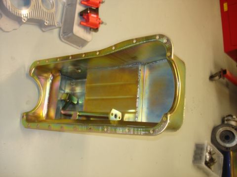 1988 Ford Mustang - A yellow-coated metal oil pan is mounted on a wall, showing its internal structure and welded seams.