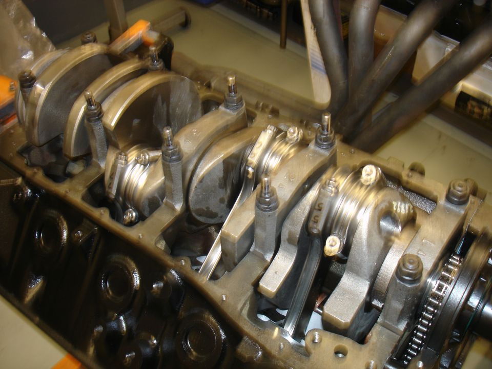 Engine block with crankshaft and connecting rods visible. Exhaust headers are in the background