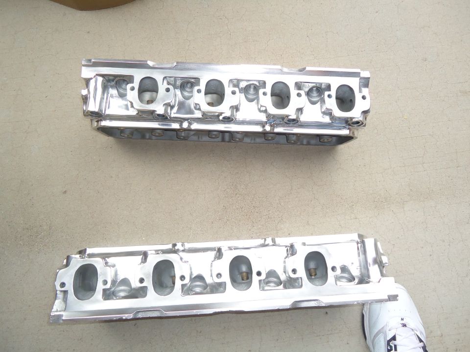 Two polished aluminum engine cylinder heads on a concrete surface