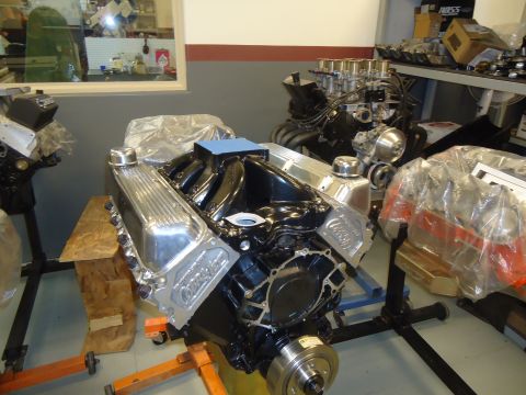1988 Ford Mustang - A black engine with chrome valve covers and intake manifold is displayed on an engine stand, with other engines visible in the background.