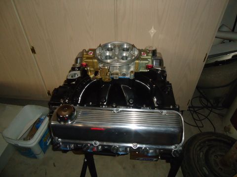 1988 Ford Mustang - A V8 engine with a dual carburetor setup is displayed on an engine stand against a wood-paneled wall.