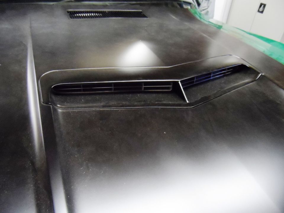 Close-up of a car's hood with a prominent scoop and vent. The hood is dark and dusty