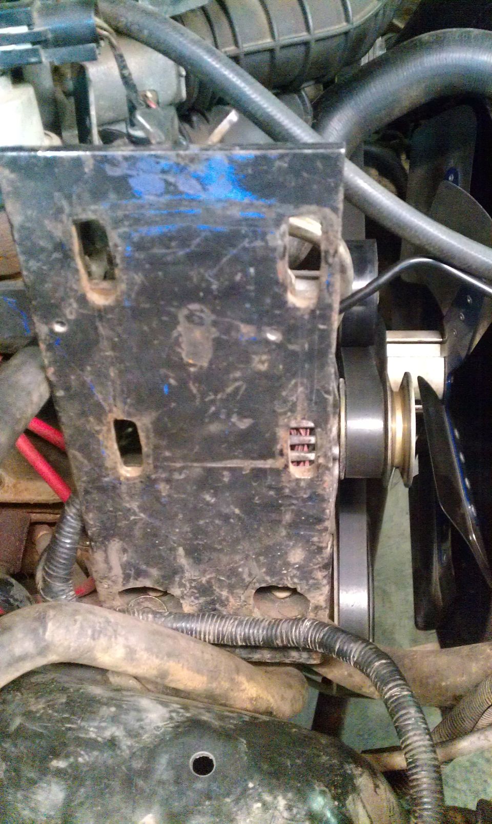 Close-up of an engine fan and black metal bracket with hoses and wiring