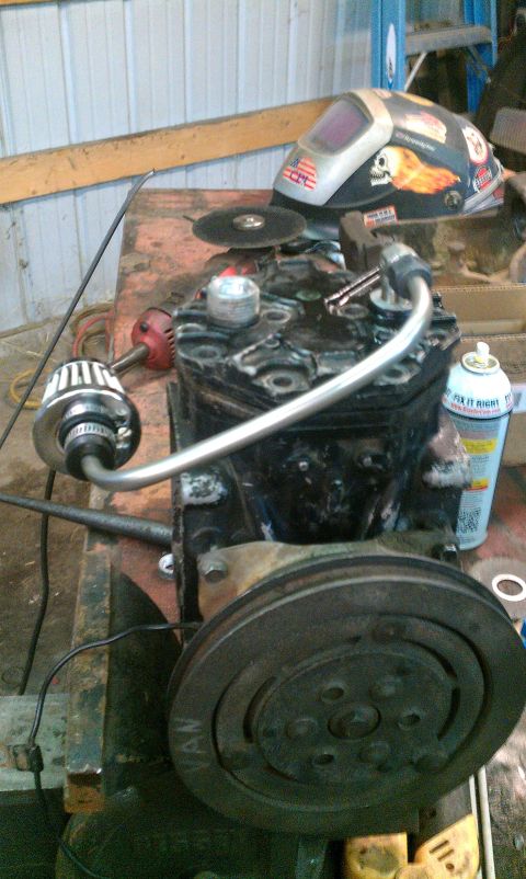 1995 Ford Bronco - A close-up of an AC compressor sits on a workbench next to a welding mask and a can of spray.