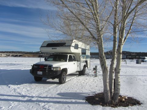 1997 Dodge 3500 - A white Dodge 3500 pickup truck with a camper shell is parked in a snowy landscape under a bright blue sky.