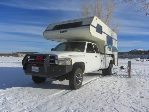 1997 Dodge 3500 - A white pickup truck with a camper shell is parked in a snowy landscape, connected to a power source.