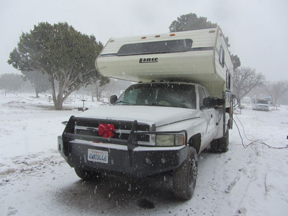 White Dodge 3500 pickup with a Lance camper, parked in snow. License plate 6HKU446