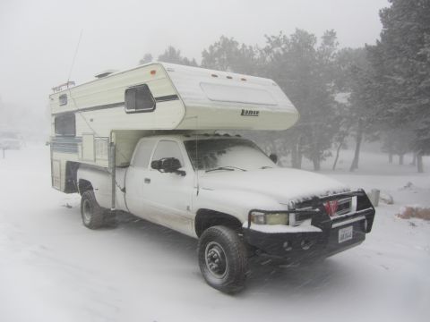 1997 Dodge 3500 - A white pickup truck with a camper shell is parked in a snowy environment, with trees in the background.