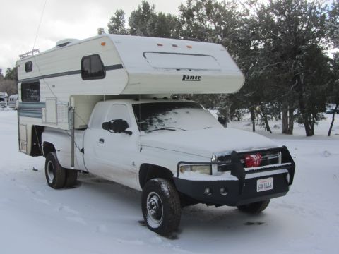 1997 Dodge 3500 - A white Dodge Ram truck with a Lance camper shell is parked in the snow, ready for a winter trip.