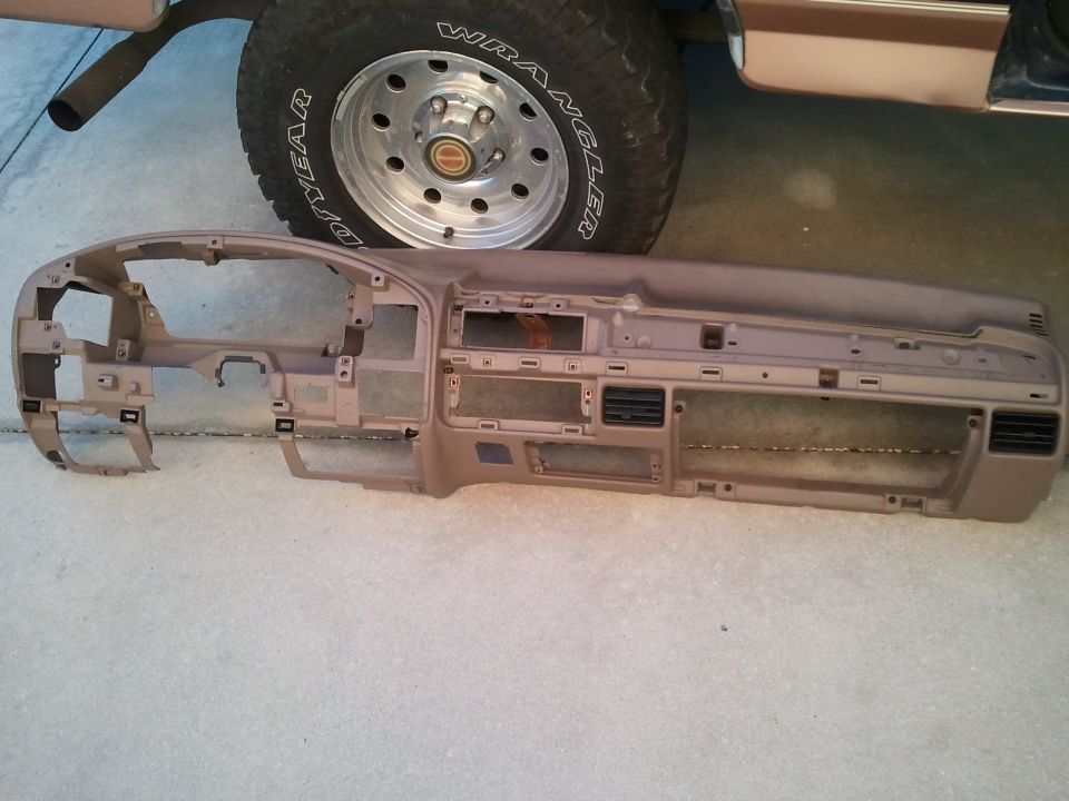removed dashboard assembly sitting on ground in front of a tire and part of a vehicle body
