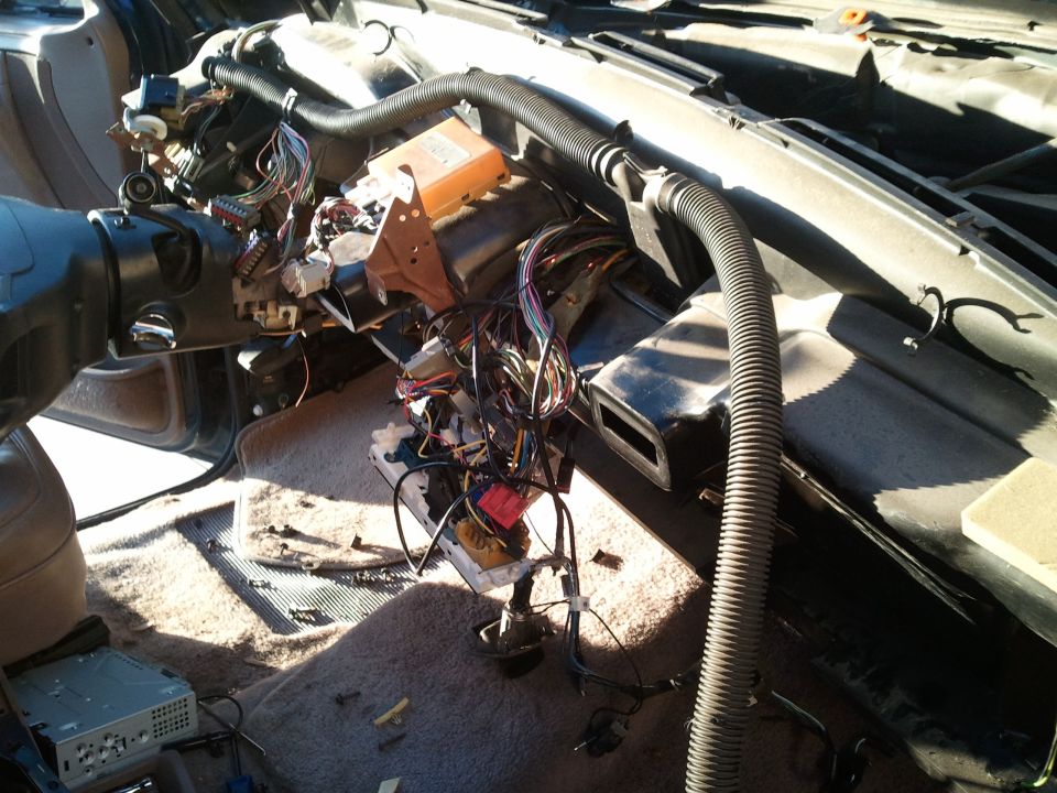 Car interior with dashboard removed, showing extensive wiring and components. Steering column visible on left