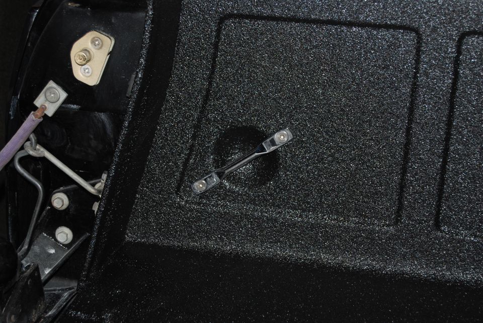 Close-up of a black textured truck bed liner with a latch mechanism visible