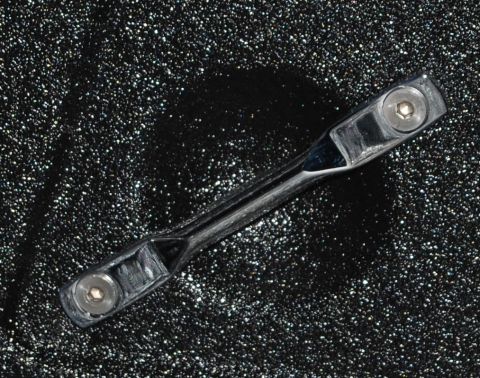 1975 Ford Ranchero - A chrome car part is shown against a black speckled background, with visible hex bolts.