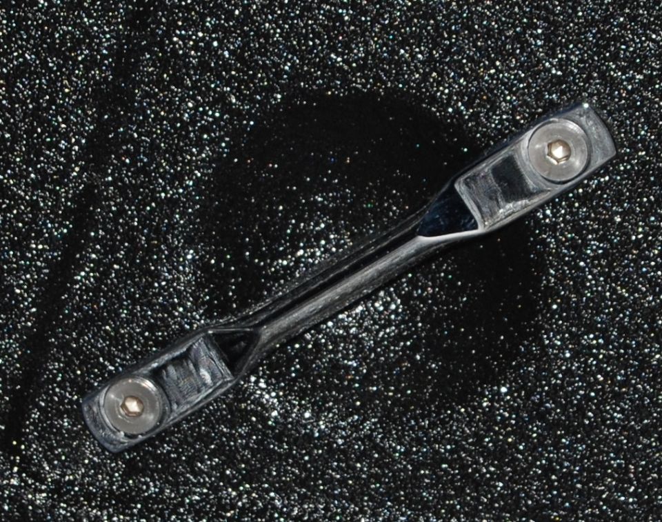 Chrome car part with two hex bolts on a black speckled background