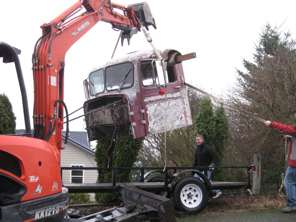 Kubota excavator lifting a truck cab off a trailer. Two men are visible