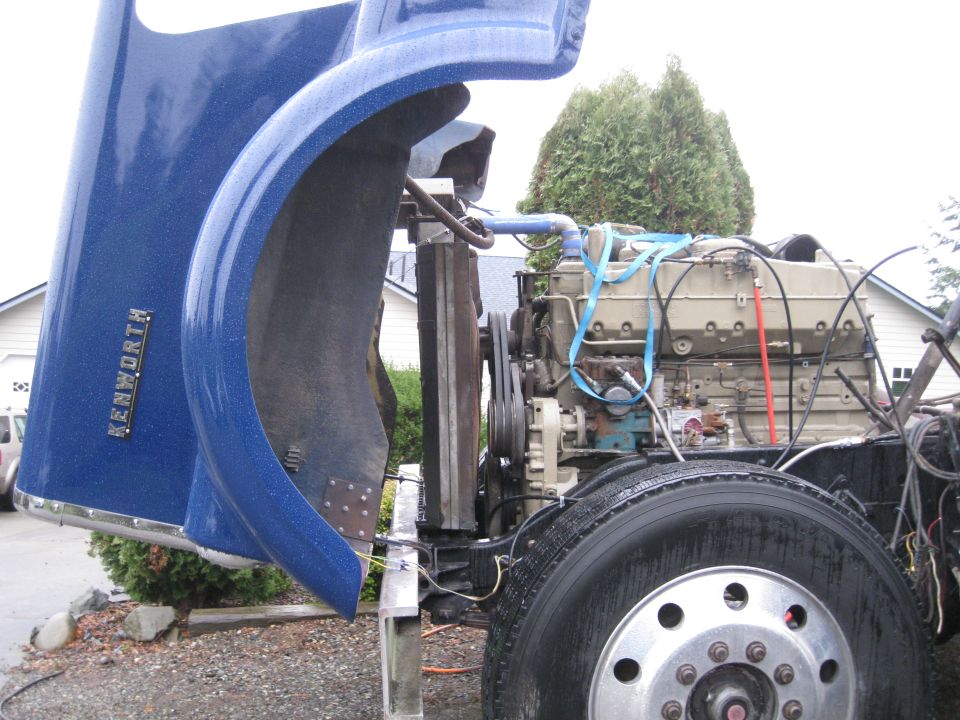 Blue Kenworth truck fender open, showing engine and radiator. Truck is parked outdoors