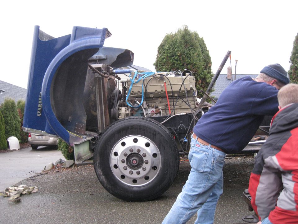 Truck engine and chassis with hood open, people working on it