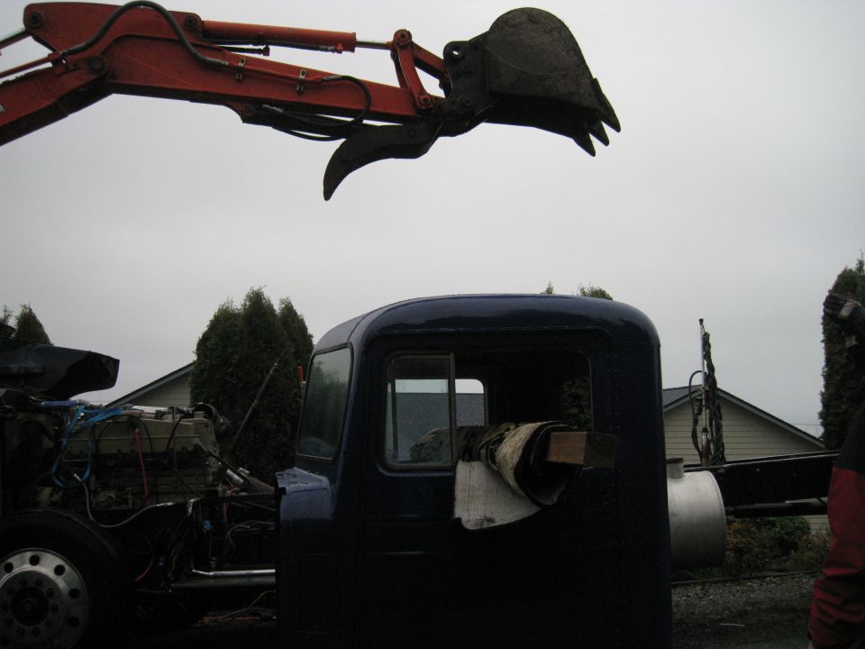 Excavator arm over dark blue truck cab. Engine visible on left