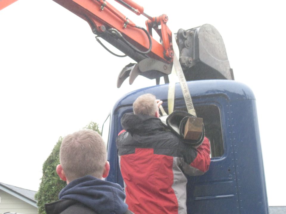 Excavator arm lifting a blue truck cab section with two people watching