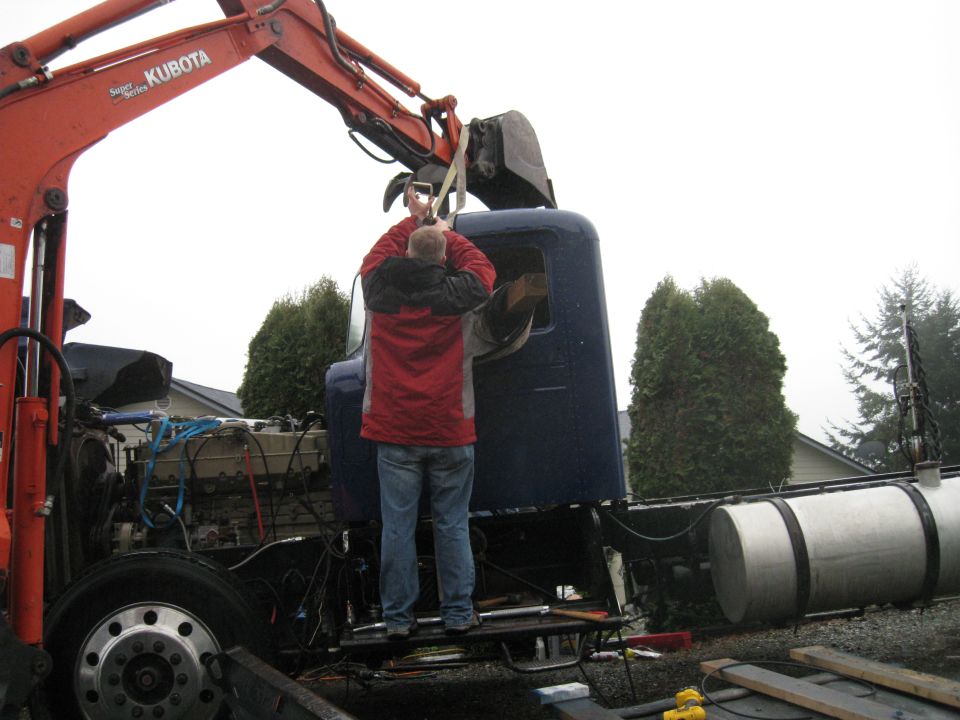 Blue truck cab with exposed engine and large fuel tanks, being worked on by a person