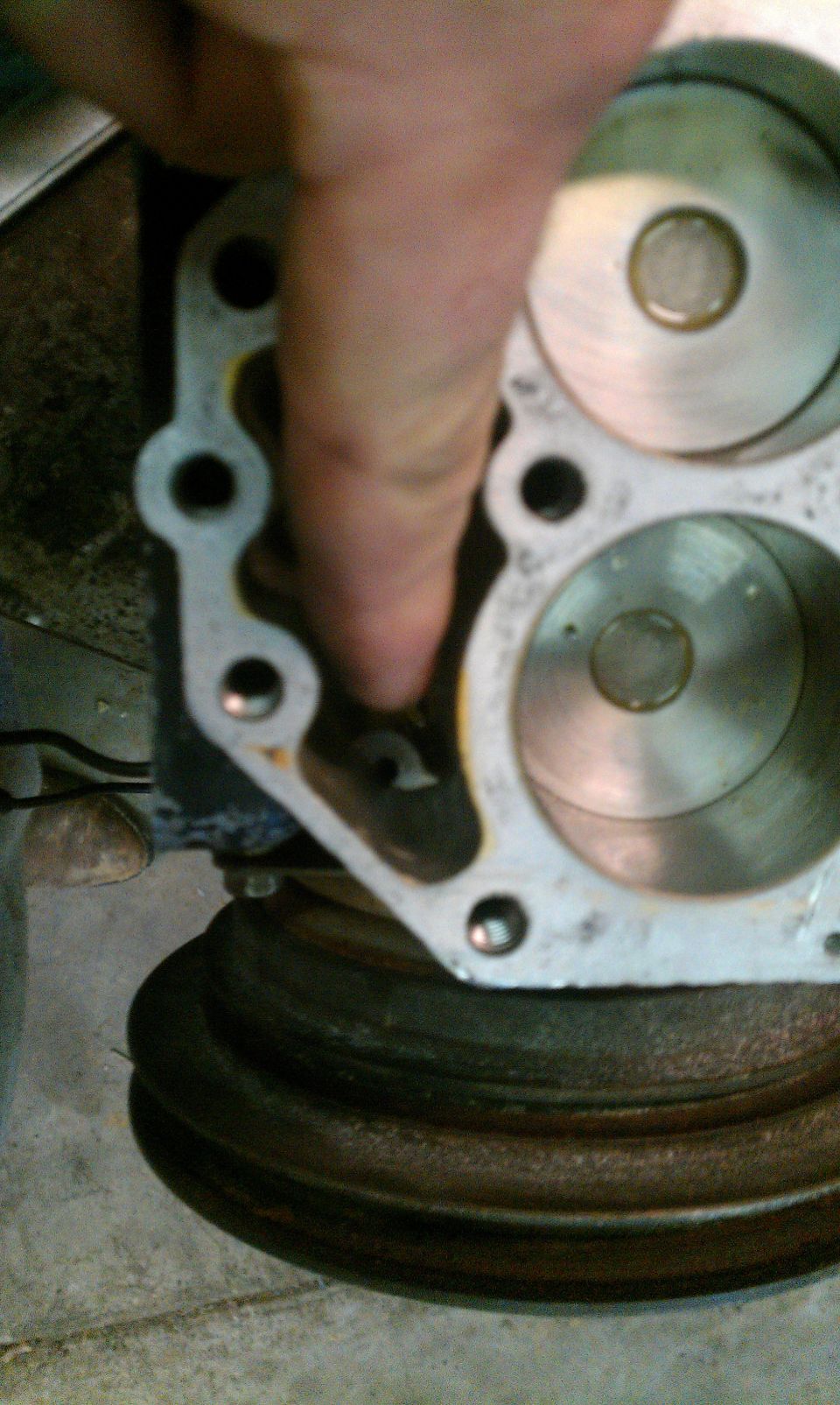 Close-up of an engine cylinder head with a finger pointing to a port, showing a valve inside