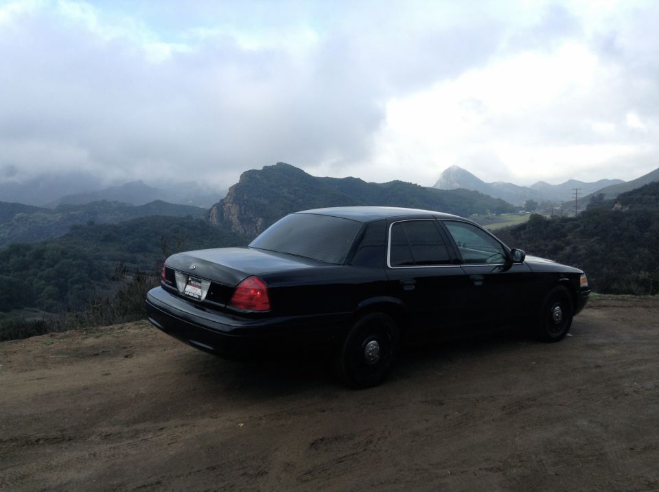 Black 2004 Ford Crown Victoria parked on a dirt road with mountains in the background