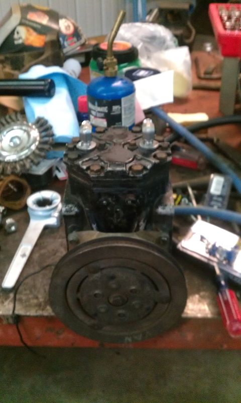 1995 Ford Bronco - An air conditioning compressor sits on a workbench next to tools and a propane torch.