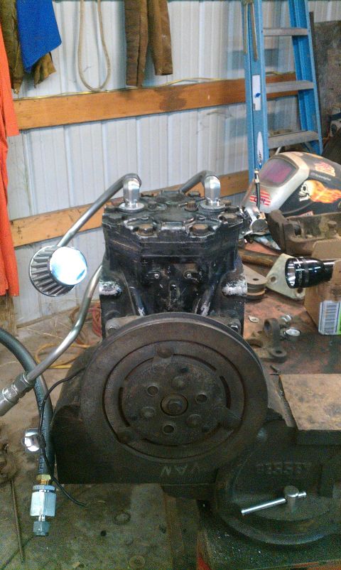 1995 Ford Bronco - An air conditioning compressor is clamped in a vise, with various hoses and a filter attached.