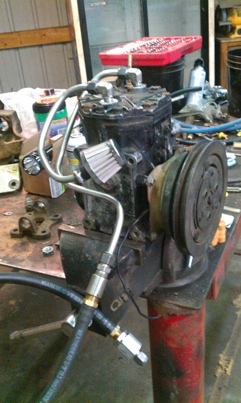 1995 Ford Bronco - An air conditioning compressor, clamped in a vise, is shown with attached hoses and a small filter.