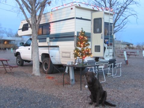 1997 Dodge 3500 - A white 1997 Dodge 3500 pickup truck with a camper shell is parked at a campsite, decorated with Christmas lights and a small tree.
