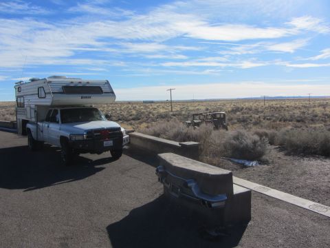 1997 Dodge 3500 - A white Dodge pickup truck with a camper shell is parked on the side of a road, with an old vehicle visible in the distance.