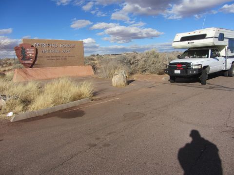 1997 Dodge 3500 - A white Dodge pickup truck with a camper shell is parked near the entrance sign for Petrified Forest National Park.