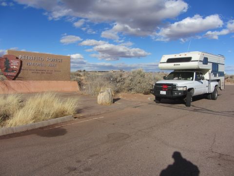 1997 Dodge 3500 - A white 1997 Dodge 3500 pickup truck with a camper shell is parked near the entrance sign for Petrified Forest National Park.